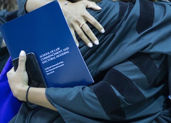 Two grads embrace as they hold a program for the Commencement ceremony