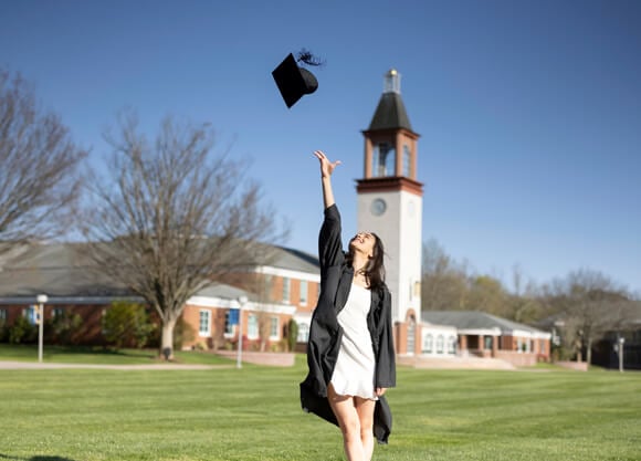 A graduate throws her cap in the air in front of the clocktower