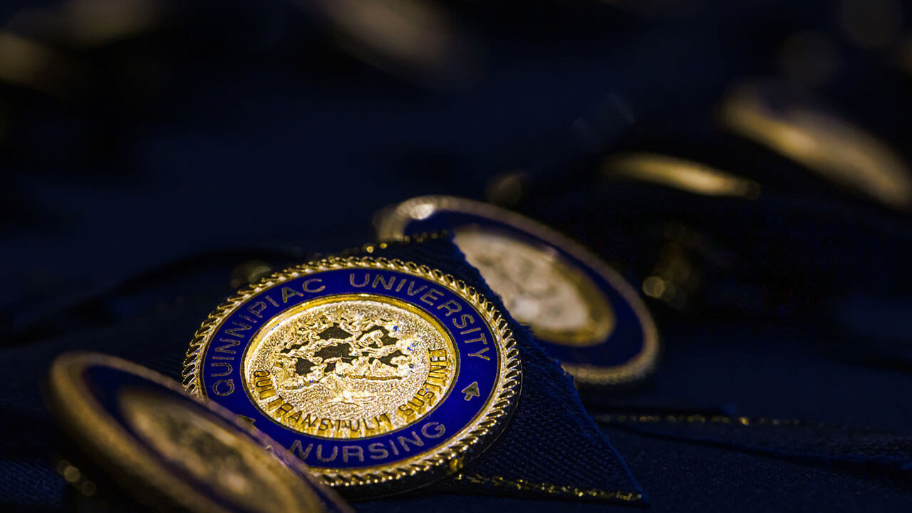 close up of a navy blue ringed gold pin reading 'Quinnipiac University Nursing' featuring the school's seal