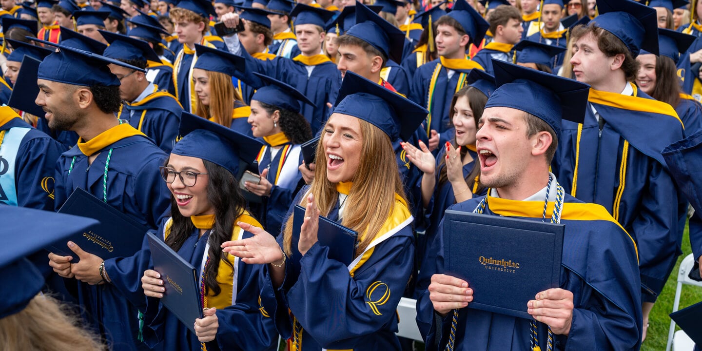 Dozens of graduates clap and cheer with their diplomas during the Quinnipiac Commencement