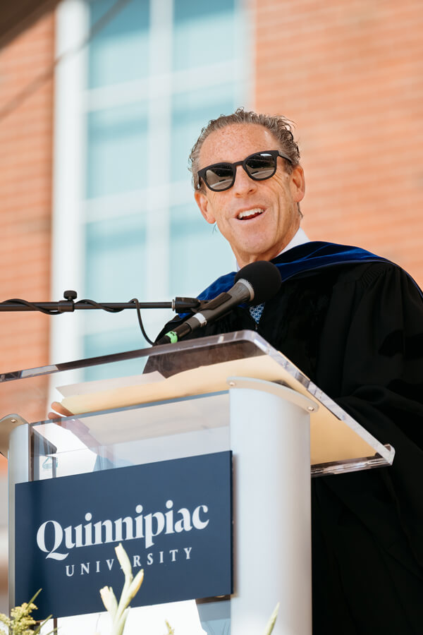 Barry Stein wears sunglasses and stands at the podium delivering remarks