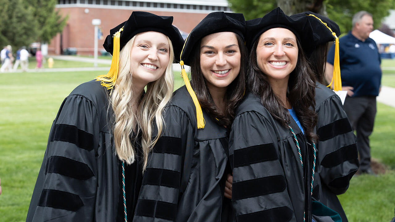 three female graduates pose together in on the quad