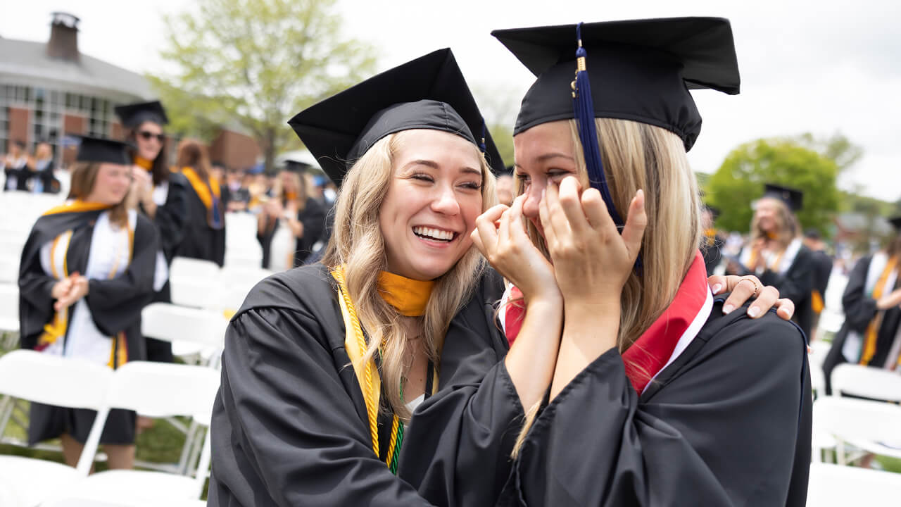 A graduate hugs her friend as she cries joyfully during Commencement